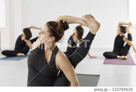 Close-up of woman in advanced yoga pose during group class session in bright room 133793610