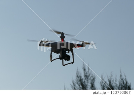 Drone with digital camera flying in the blue sky at sunset. Drone with digital camera flying in the blue sky at sunset. 133793867