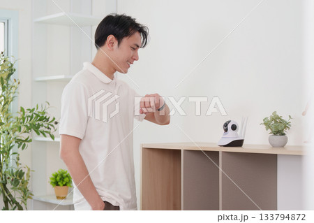 Technology and Lifestyle. Young man interacting with smart home device while checking his smartwatch. Technology and Lifestyle. Young man interacting with smart home device while checking his smartwatch. 133794872