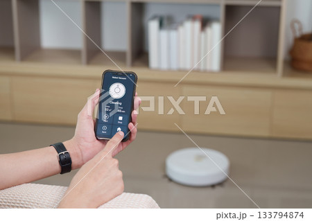 Technology and Lifestyle. User controlling robotic vacuum with smartphone app for efficient cleaning. Technology and Lifestyle. User controlling robotic vacuum with smartphone app for efficient cleaning. 133794874