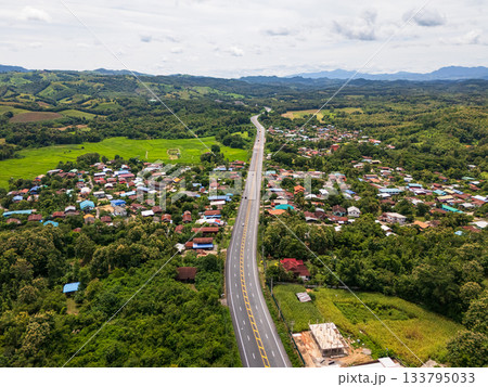Aerial drone view of Highway winding through lush green mountains between Nan, Thailand. A scenic landscape of the road surrounded by tropical forest and a peaceful countryside Aerial drone view of Highway winding through lush green mountains between Nan, Thailand. A scenic landscape of the road surrounded by tropical forest and a peaceful countryside 133795033
