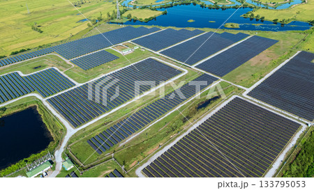 Drone shot aerial view solar energy array provides renewable power in large scale facility surrounded by greenery and water in rural place. Solar farm at the countryside Drone shot aerial view solar energy array provides renewable power in large scale facility surrounded by greenery and water in rural place. Solar farm at the countryside 133795053