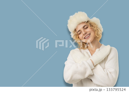 Woman smiling while wearing a white sweater and fluffy hat Woman smiling while wearing a white sweater and fluffy hat 133795524