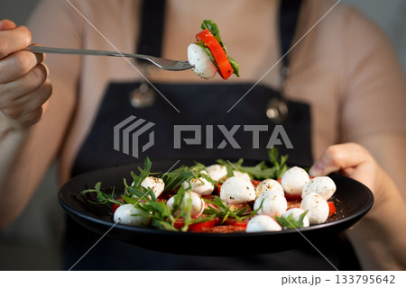 Eating Caprese Salad With Fork in Kitchen at Noon 133795642