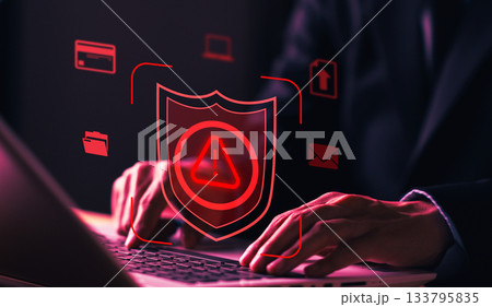 Cybersecurity concept with shield alert icon and man working on laptop, representing data protection, system security, cyber attack prevention, and digital defense. 133795835