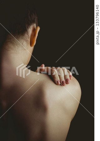 bare-shouldered woman is being shown from behind in flat portrait with dark backdrop, copy space 133796140