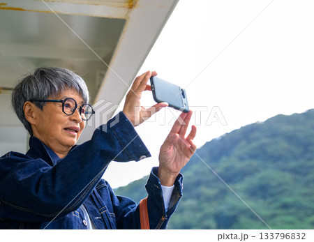 スマホで山々を撮影する眼鏡のシニア女性、島根・隠岐の島への船旅 スマホで山々を撮影する眼鏡のシニア女性、島根・隠岐の島への船旅 133796832