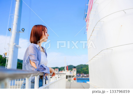 フェリーデッキで海を眺める若い女性と乗客たち、秋の旅行の始まり フェリーデッキで海を眺める若い女性と乗客たち、秋の旅行の始まり 133796859