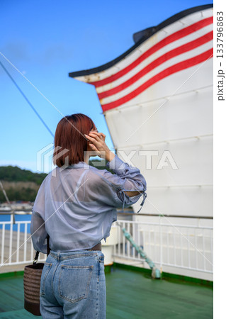 フェリー甲板から海と島を眺める若い女性の後ろ姿、青空と船体 133796863