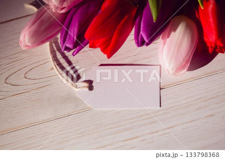 Tulip cluster is casting soft shadows on wooden tabletop in flat design, with blank gift tag Tulip cluster is casting soft shadows on wooden tabletop in flat design, with blank gift tag 133798368