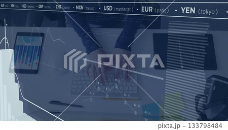 Typing woman's hands navigating financial chart overlays on white desk, with tablet and headphones 133798484