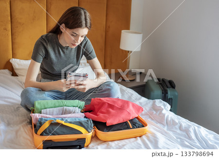 Woman preparing for travel, organizing clothes in suitcase on bed Woman preparing for travel, organizing clothes in suitcase on bed 133798694