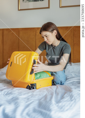 Young woman packing yellow suitcase on hotel bed 133798695