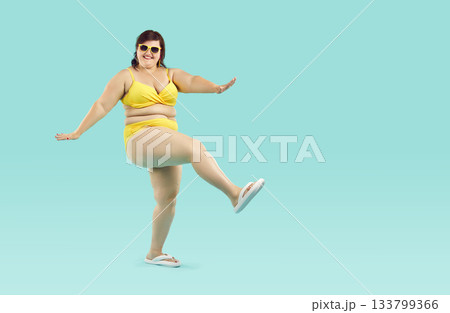 Funny young fat woman in yellow bikini and sunglasses having fun isolated on blue background. Funny young fat woman in yellow bikini and sunglasses having fun isolated on blue background. 133799366