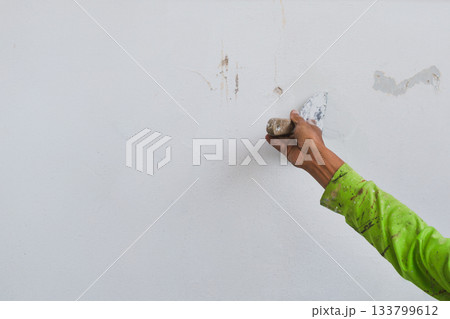Man hand with trowel plastering a house wall outside. Man hand with trowel plastering a house wall outside. 133799612