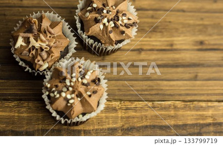 Flat design is showing three chocolate cupcakes with swirled frosting and sprinkles on wooden table Flat design is showing three chocolate cupcakes with swirled frosting and sprinkles on wooden table 133799719