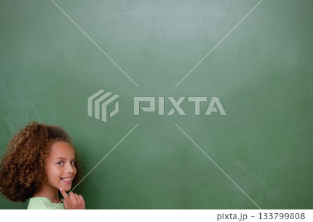 Smiling schoolgirl is standing before full-wall green chalkboard in flat design, copy space 133799808