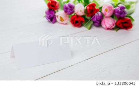 Flat design blank folded card is sitting on white plank surface, featuring colorful tulip bouquet 133800043