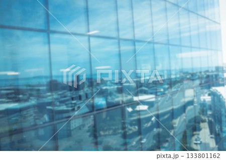 Defocussed image of modern cityscape and blue sky reflected in glass building, with copy space 133801162