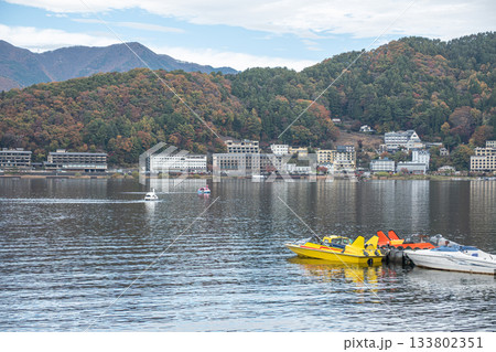 Lake Kawaguchi, Fujikawaguchiko, Minamitsuru District, Yamanashi, Japan, Yellow pedal boats docked on lake with mountains and town in background 133802351