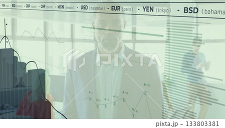 Standing African American man analyzing digital charts on office glass wall showing currency ticker Standing African American man analyzing digital charts on office glass wall showing currency ticker 133803381