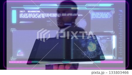 Holding laptop, male wearing suit and tie examining holographic panels in office, viewing code 133803466