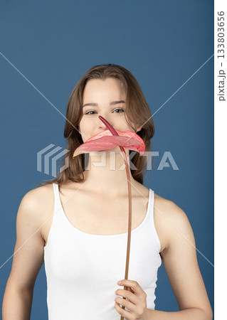 Beautiful woman with pink Anthurium flower against blue background Beautiful woman with pink Anthurium flower against blue background 133803656