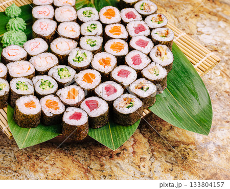Delicious sushi rolls arranged on a bamboo plate with green garnish Delicious sushi rolls arranged on a bamboo plate with green garnish 133804157