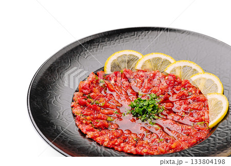 Freshly prepared beef tartare served with lemon and herbs on a black plate 133804198