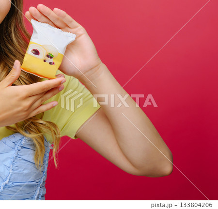 Delicious dessert treat held by a happy person against a vibrant red background 133804206