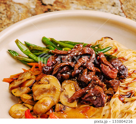 Delicious stir-fried beef with vegetables and noodles served on a plate Delicious stir-fried beef with vegetables and noodles served on a plate 133804216
