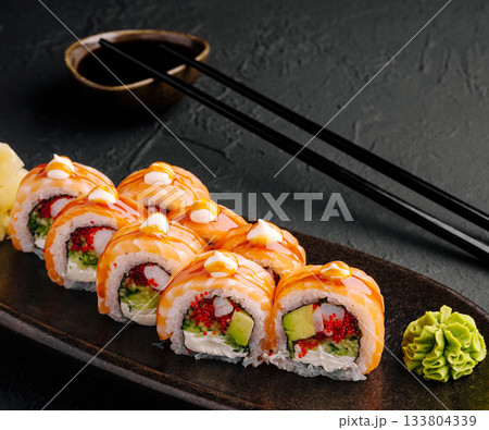 Colorful sushi rolls arranged neatly on a dark plate with wasabi and sauce Colorful sushi rolls arranged neatly on a dark plate with wasabi and sauce 133804339