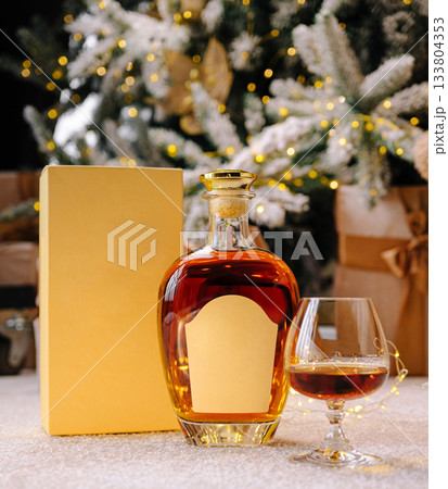 Festive whiskey bottle and glass by a Christmas tree with gifts 133804353