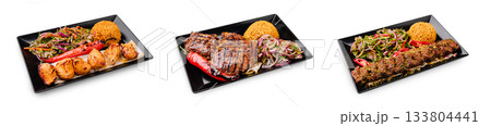 Grilled meat dishes served on black plates with colorful sides and rice 133804441