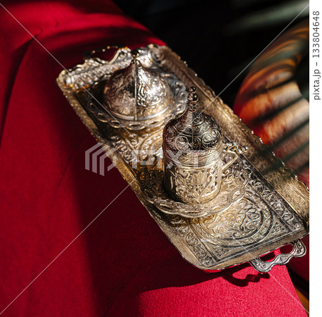 Traditional silver coffee set displayed on a vibrant red tablecloth 133804648