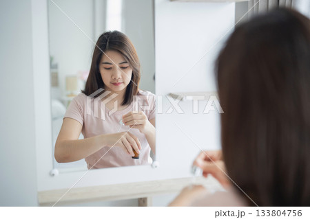 Young Woman Applying Skincare Product in Modern Bathroom Mirror Reflection, Emphasizing Self-Care and Daily Beauty Routine 133804756