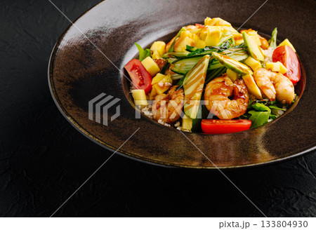 Shrimp salad with fresh vegetables, mango, and herbs served in a shallow bowl 133804930