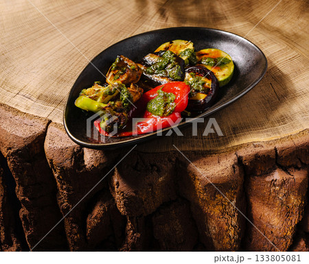 Grilled vegetables served on a sleek black plate with wooden background Grilled vegetables served on a sleek black plate with wooden background 133805081