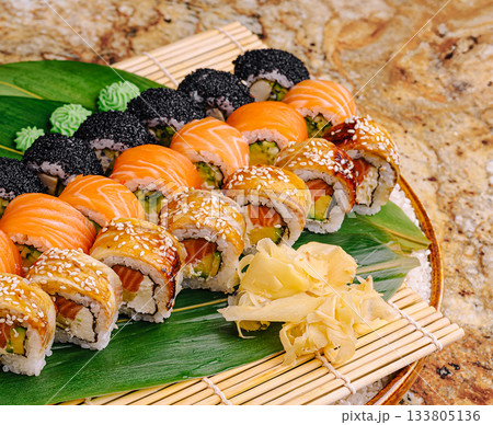 Sushi platter with various rolls arranged on bamboo mat and green leaves Sushi platter with various rolls arranged on bamboo mat and green leaves 133805136