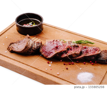 Deliciously cooked beef meat served on a wooden board with sauce and herbs Deliciously cooked beef meat served on a wooden board with sauce and herbs 133805208