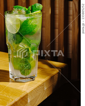 Refreshing mojito with mint and lime on wooden table in cozy setting Refreshing mojito with mint and lime on wooden table in cozy setting 133805252