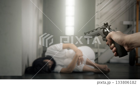 Human hand holding a revolver handgun in front of a woman in distress, sitting on the floor with her face hidden. Concept of gun violence Human hand holding a revolver handgun in front of a woman in distress, sitting on the floor with her face hidden. Concept of gun violence 133806182
