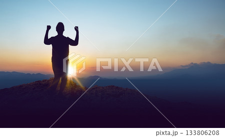 Silhouette of a person standing on a hilltop with arms raised in celebration against the sunrise background. Concept of a winner Silhouette of a person standing on a hilltop with arms raised in celebration against the sunrise background. Concept of a winner 133806208