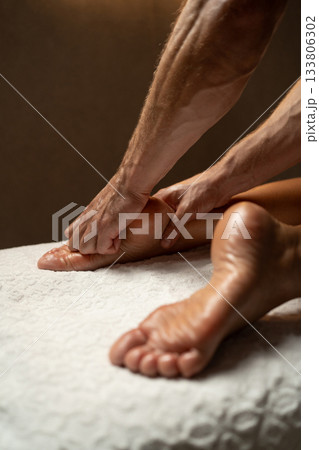 Close-up of a professional therapist performing a relaxing foot and leg massage in a spa, with oil on the skin, promoting wellness, relaxation, and circulation in a calm atmosphere. 133806302