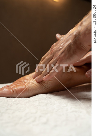 Close-up of a foot massage in a spa, therapist gently massaging the heel with oil, relaxation and wellness concept, warm light atmosphere, skin care and body therapy. 133806324