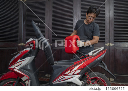 Indonesian southeast asian repairman refilling the gasoline fuel into the tank after repairing a motorcycle in a workshop 133806725