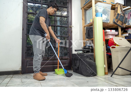 Indonesian southeast asian man sweeping the floor with a broom and a dustpan. Cleaning home activity 133806726