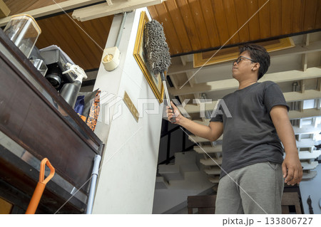 Indonesian southeast asian man is cleaning dust from a picture frame using a duster. Cleaning home activity 133806727