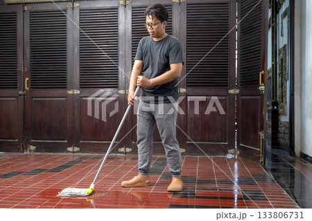 Indonesian southeast asian man is cleaning the floor with a mop. Cleaning home activity Indonesian southeast asian man is cleaning the floor with a mop. Cleaning home activity 133806731