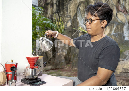 Indonesian southeast asian man pouring coffee beans into a scale cup for making coffee with the V60 pour over method on an outdoor background. Making coffee activity 133806757